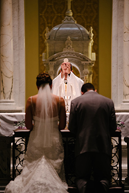 Couple kneeling before the altar as the priest raises a Host